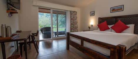 A bedroom with a wooden bed, a desk, and a chair. There is a balcony with a view of greenery.