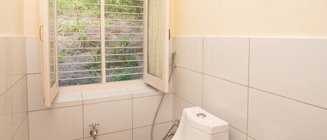 A small bathroom with a toilet, a window, a trash can, and a towel rack.