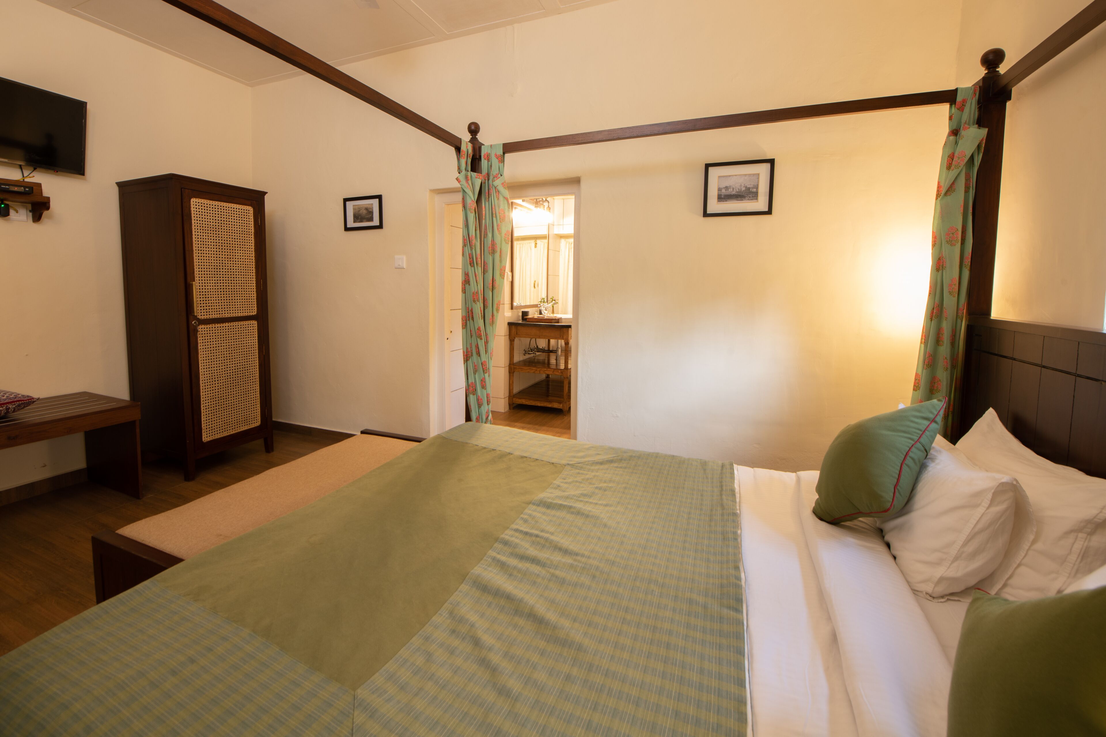 A four-poster bed with a green and white checkered bedspread, a wooden wardrobe, and a small bedside table.