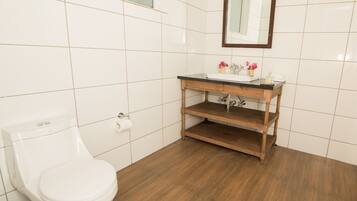 A bathroom with a toilet, a wooden vanity with a sink, and a mirror.