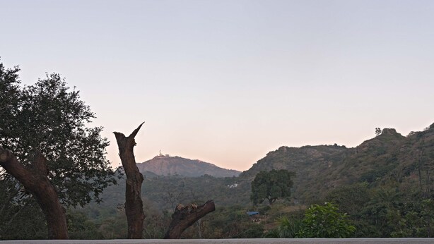 Un área de comedor al aire libre con sillas de mimbre y una mesa, un brasero, y una vista panorámica de colinas y árboles.