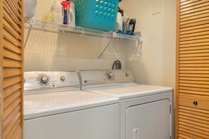 A laundry area with two white washing machines, a shelf with cleaning supplies, and a blue laundry basket. - West Vail Ptarmigan Townhome - Hot Tub & Easy Bus (Vail)