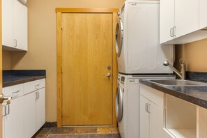 A compact kitchen with a wooden door, white cabinets, a washing machine, and a sink. - Large East Vail Home - Steps to Bus & Gore Creek (Vail)