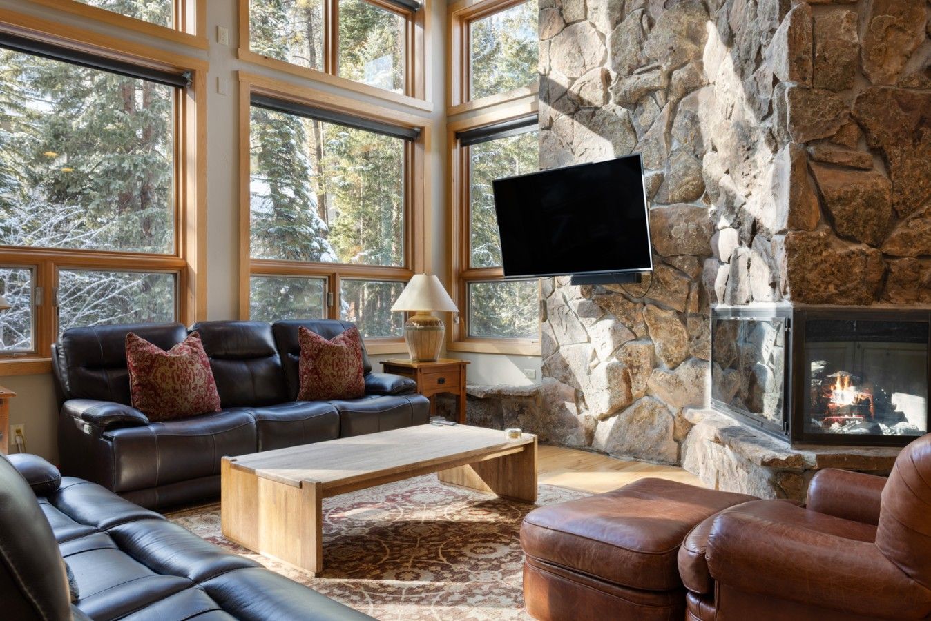 A cozy living room with a stone wall, a fireplace, a television, and leather furniture.