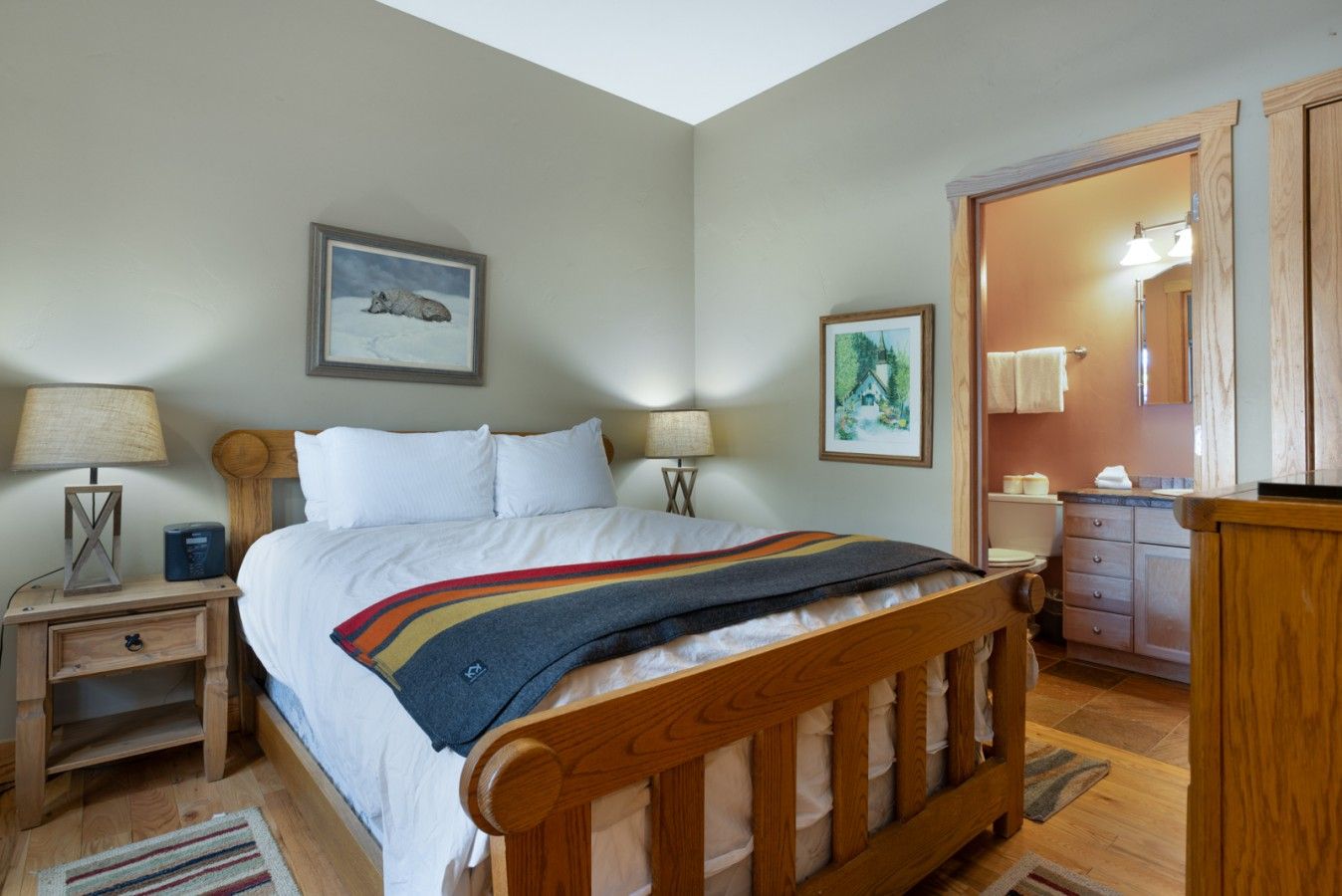 Quarto com cama de madeira, duas mesas de cabeceira com luminárias, um criado-mudo, cômoda de madeira e um espelho.