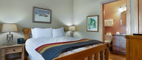 Quarto com cama de madeira, duas mesas de cabeceira com luminárias, um criado-mudo, cômoda de madeira e um espelho.