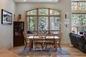 A dining area with a table and chairs, a large window with a view of trees, a cabinet, and a couch.