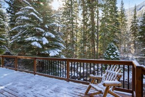 A wooden deck with snow-covered chairs and a railing overlooking a forested area with tall evergreen trees. - Large East Vail Home - Steps to Bus & Gore Creek (Vail)