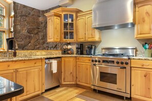 A kitchen with wooden cabinets, a stone wall, a stainless steel stove, and a coffee maker. - Large East Vail Home - Steps to Bus & Gore Creek (Vail)