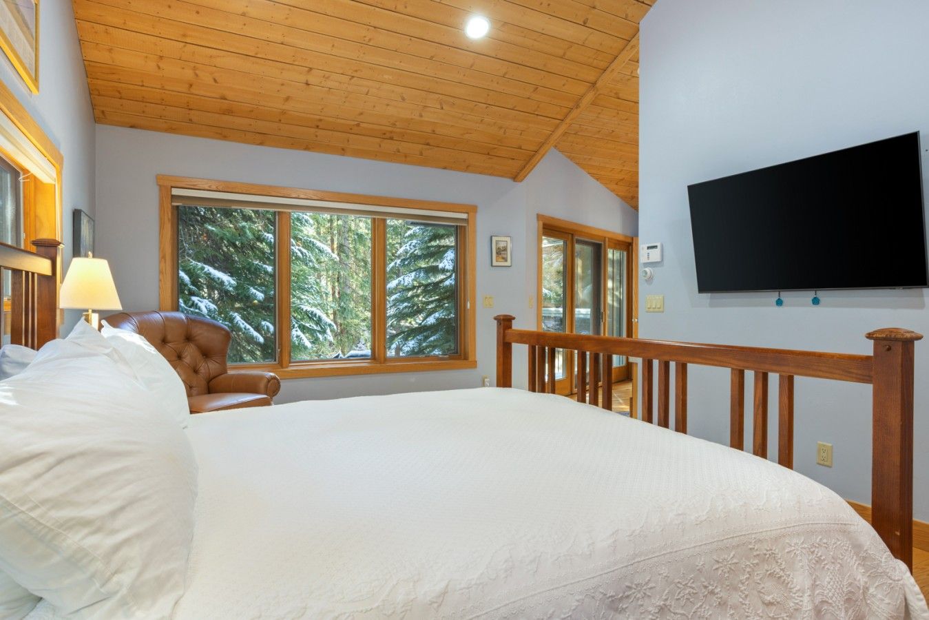 A bedroom with a large bed, wooden headboard, a television mounted on the wall, and a window with a view of trees.