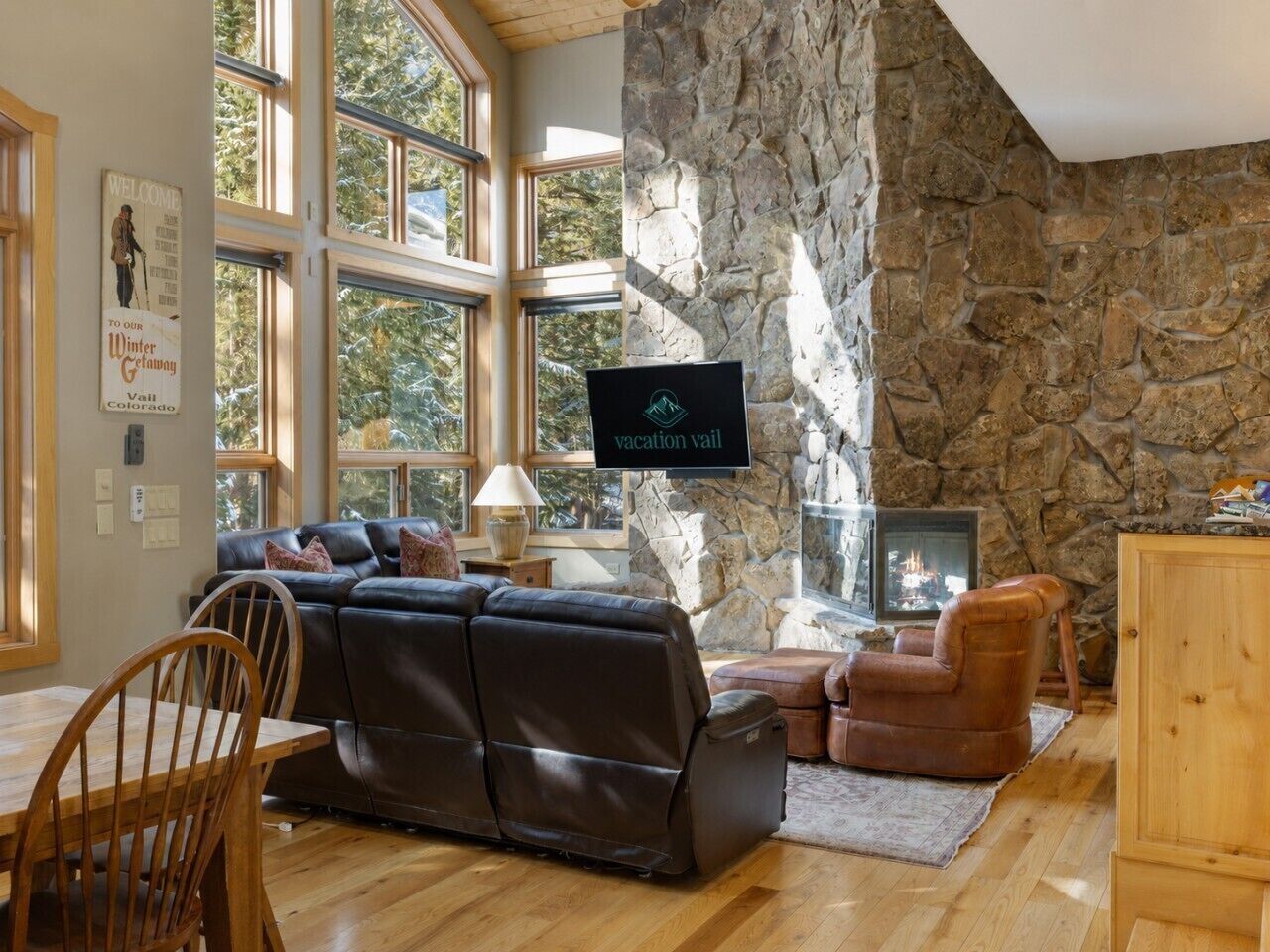 A cozy living room with a stone wall, a fireplace, a television, and a large window.