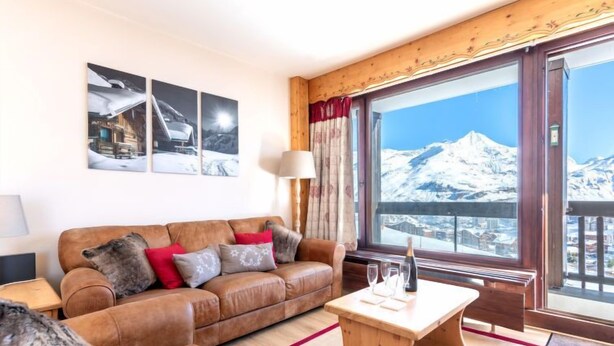Un salón acogedor con un sofá de cuero marrón, una mesa de centro de madera y un ventanal con vistas a la montaña.