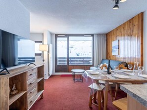 Quarto de hotel moderno com área de jantar, televisão, painéis de madeira e vista para o exterior.