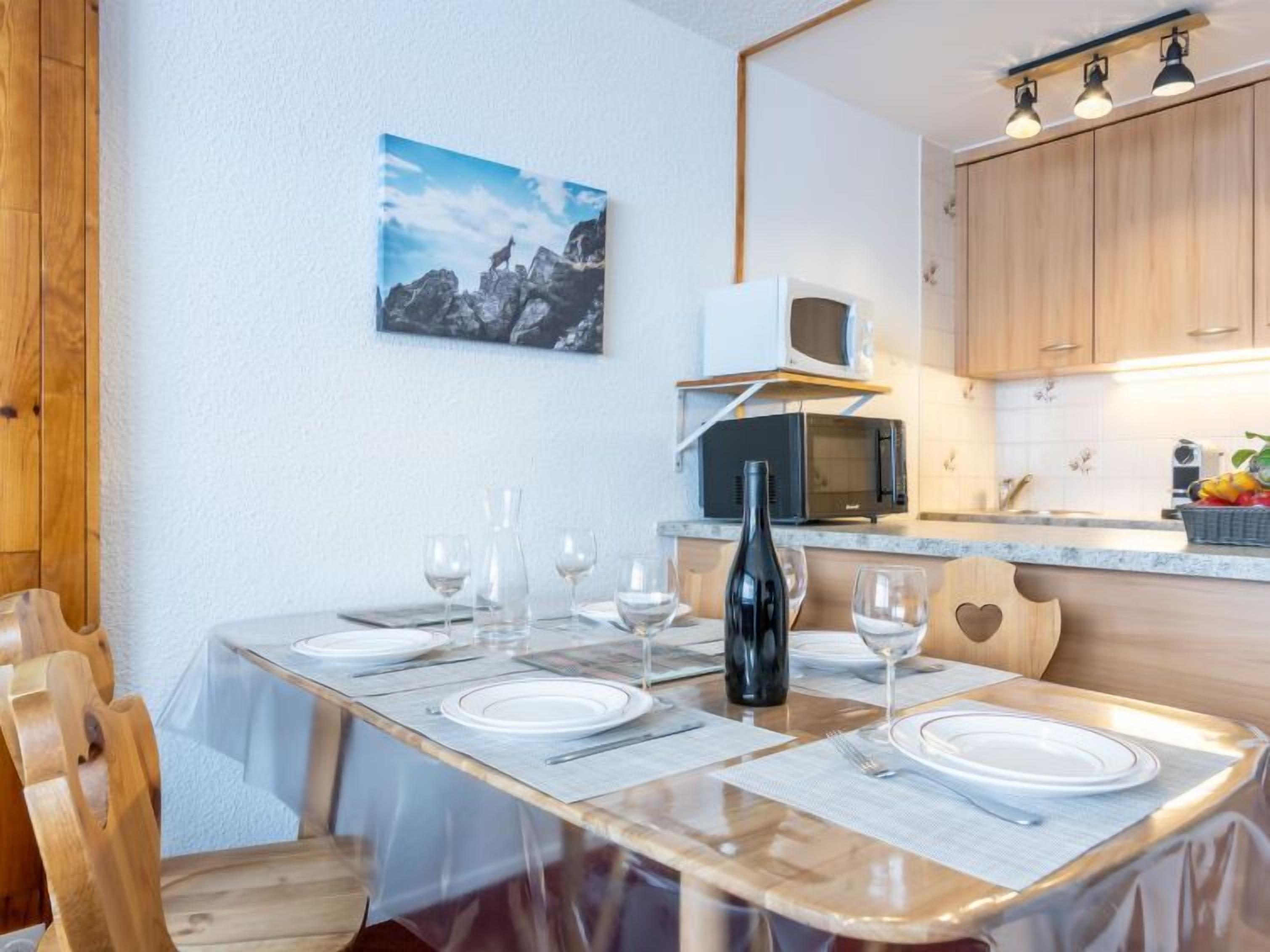 A dining area with a wooden table set for four, a black wine bottle, and a painting on the wall.