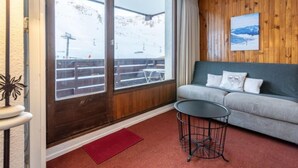 Ein gemütliches Zimmer mit einer Couch, einem kleinen runden Tisch und Blick auf eine verschneite Landschaft mit Holzboden und Skilift.