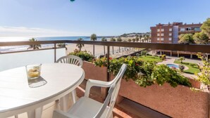 Un balcon avec une table et des chaises, donnant sur une plage et un jardin aménagé.