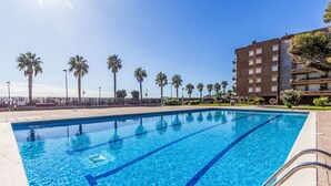 Une piscine à l’eau d’un bleu cristallin, entourée de palmiers et bordée d’un bâtiment doté de nombreux balcons.