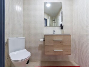 Un baño con inodoro blanco, tocador de madera con espejo y pared con azulejos.