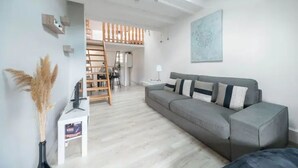 A modern living room with a grey sofa, a white side table, a ladder, and a painting on the wall.