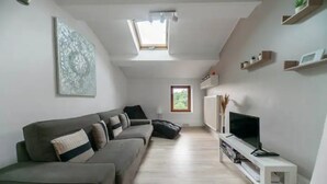 A modern living room with a grey sofa, a flat-screen TV, and a skylight.
