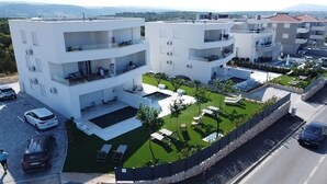 A modern multi-story residential building with balconies, a swimming pool, and a well-maintained lawn. - Apartments Twins with pools (Novalja)