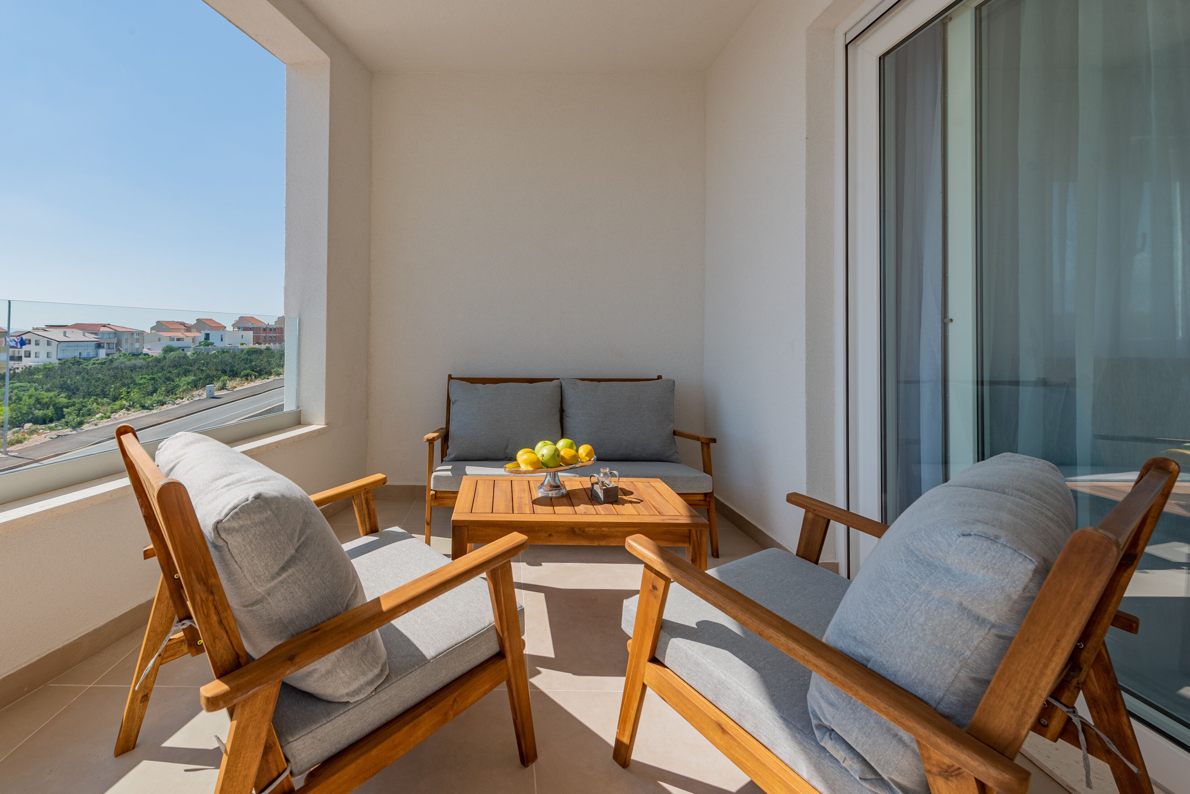 Un balcon avec des meubles en bois, une table garnie de fruits et une vue sur des bâtiments et de la verdure.