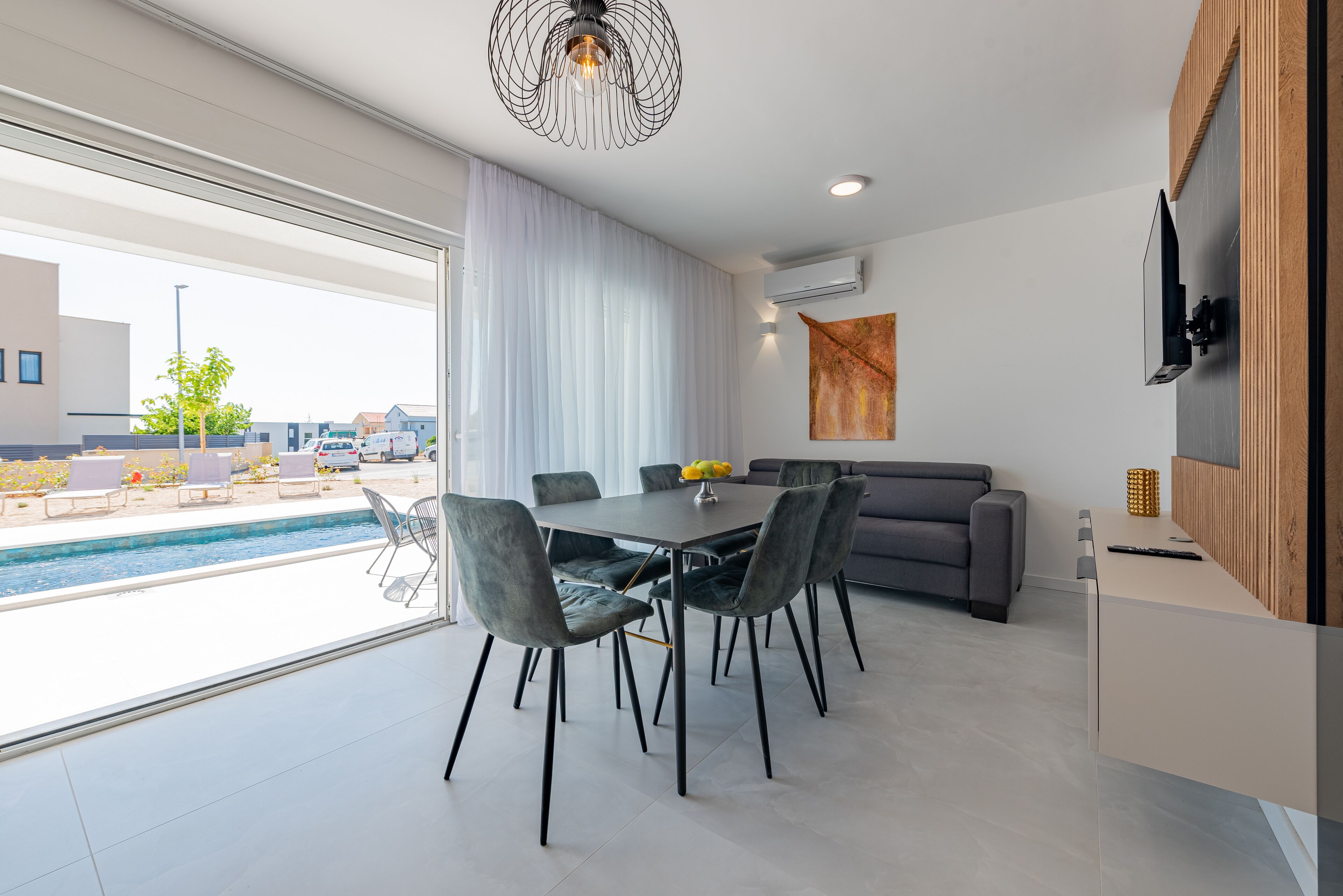 A modern kitchen with a dining area, a grey sofa, and a TV mounted on the wall.