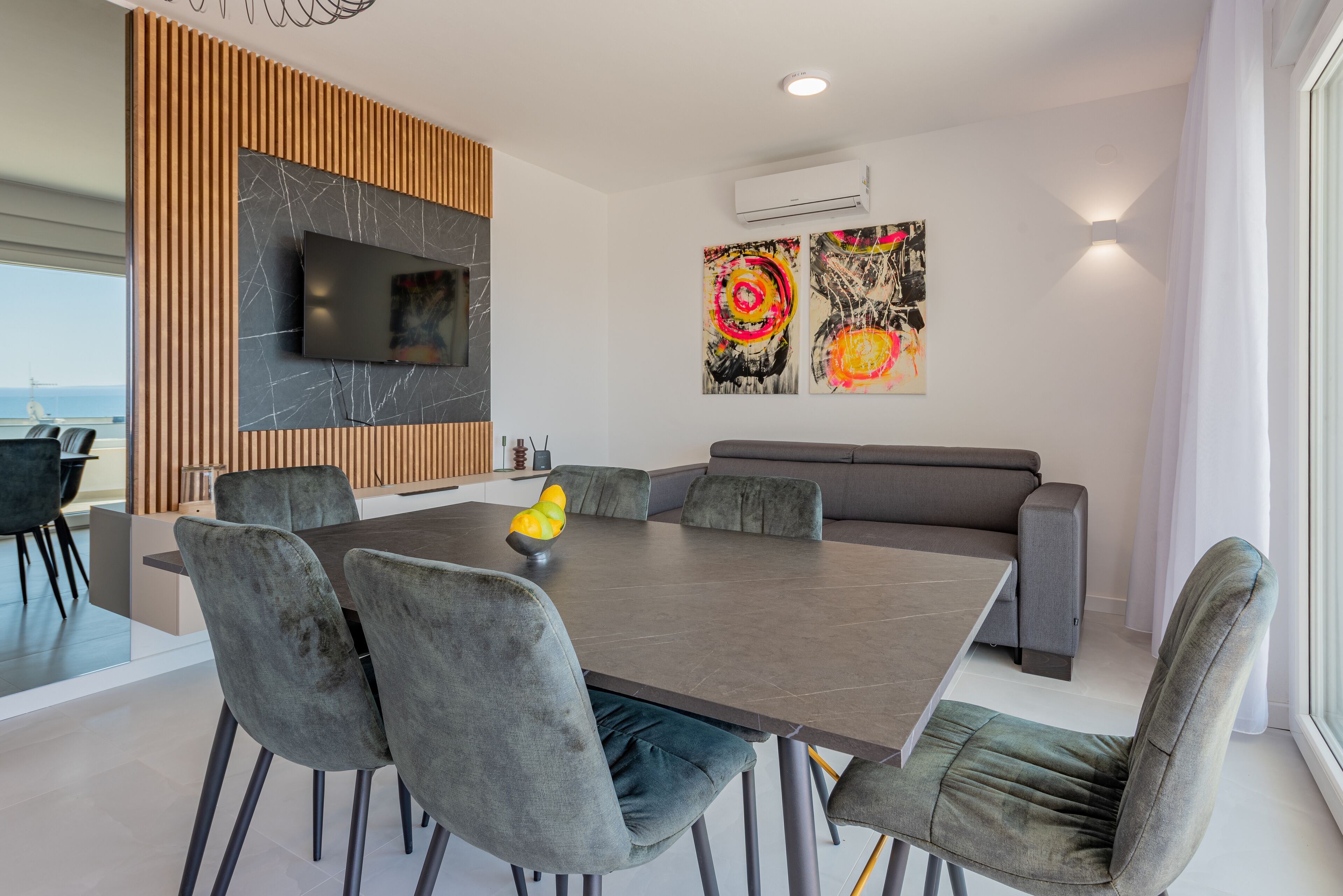 Un espace repas moderne avec une grande table, des chaises à revêtement gris et un canapé gris.