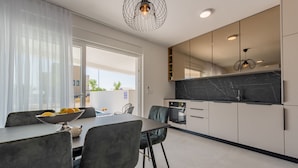A modern kitchen with a marble countertop, built-in oven, and a dining area with a table and chairs. - Apartments Twins with pools (Novalja)