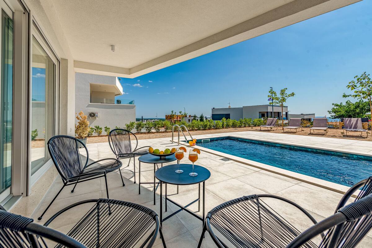 A poolside area with a table and chairs, a pool, and a view of the surrounding buildings.