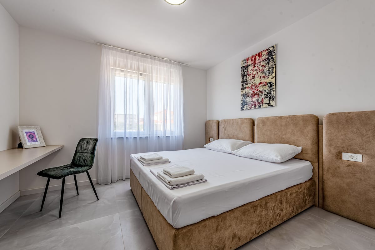 A bedroom with a bed, a chair, a desk, and a window with curtains.