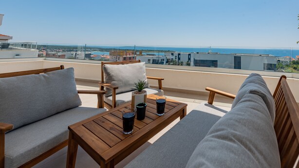 A balcony with a wooden table, two sofas, and a potted plant. - Apartments Twins with pools (Novalja)
