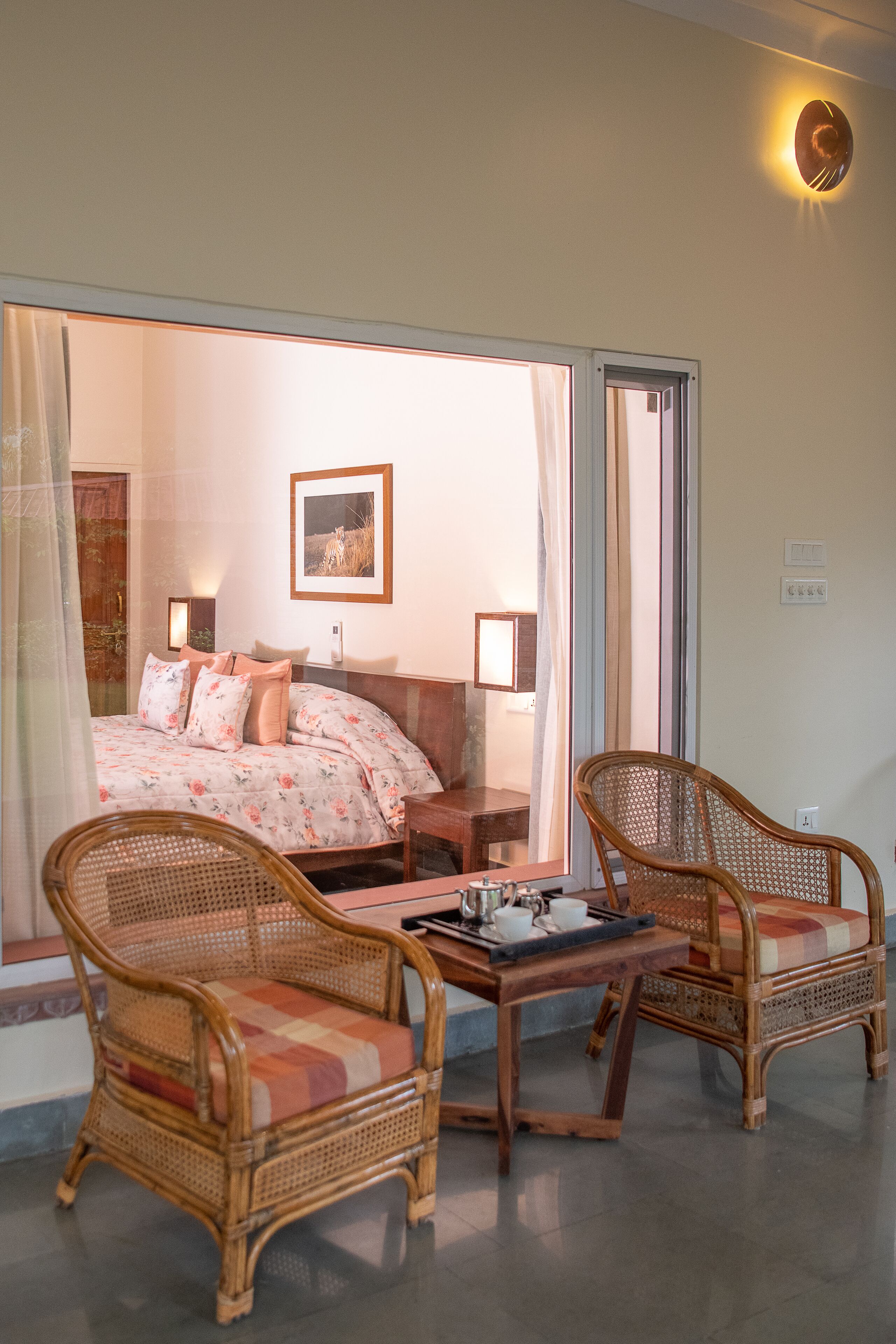 A room with a bed, two wicker chairs, a small table, and a window with curtains.