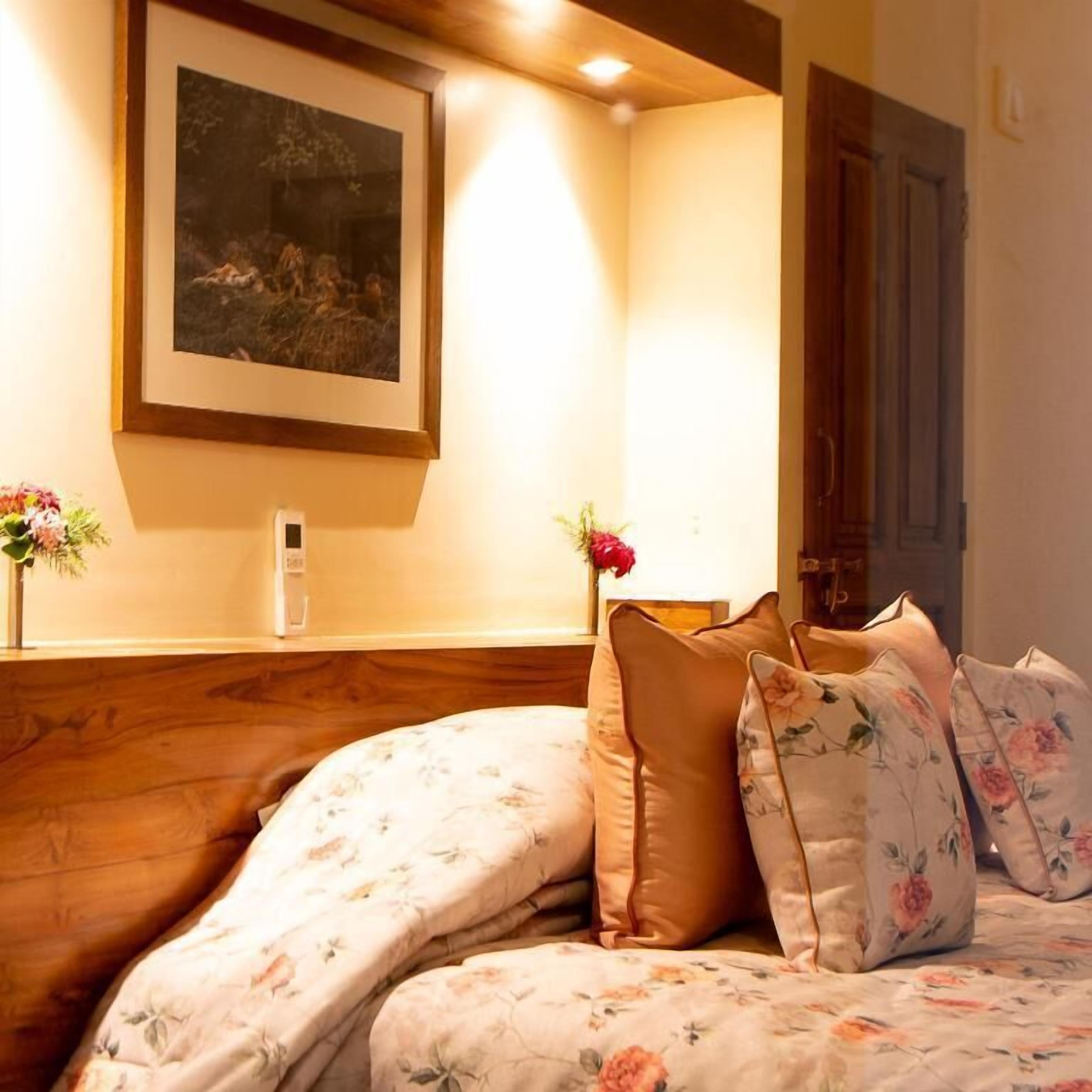 A bedroom with a curved bed, floral bedding, a framed picture on the wall, and a bedside table with a vase of flowers.