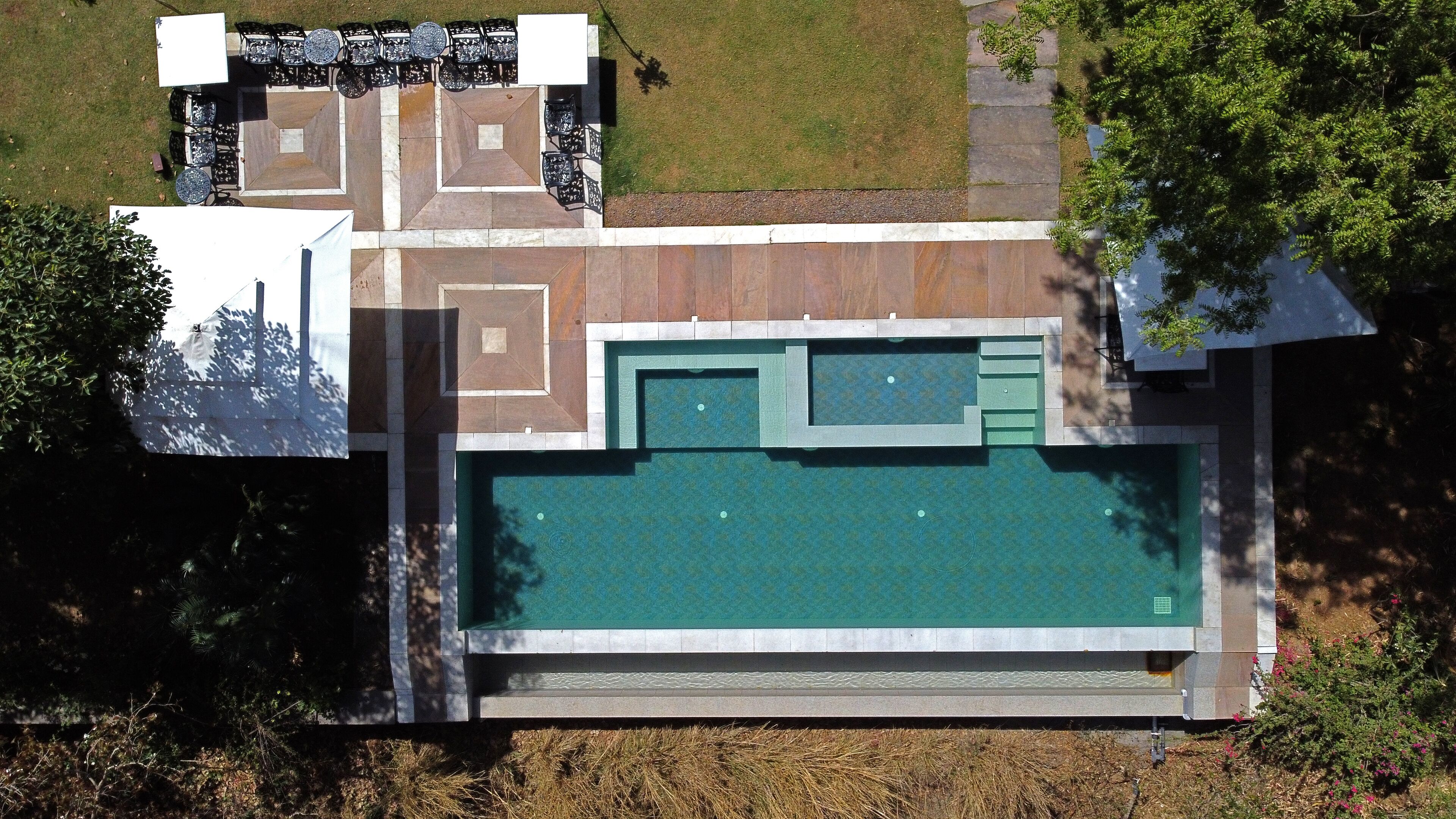 An aerial view of a property with a swimming pool, outdoor seating area, and a landscaped garden.
