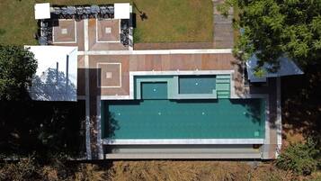 An aerial view of a property with a swimming pool, outdoor seating area, and a landscaped garden.