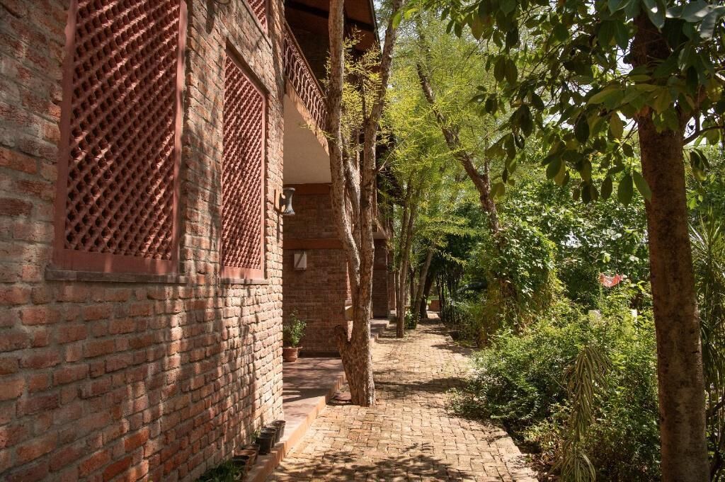 A brick building with a covered walkway lined with trees and plants.