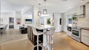 A modern kitchen with a central island, bar stools, stainless steel appliances, and pendant lighting. - Lakefront Family Fun Home with Private Dock 3BR 2B (Fort Lauderdale)