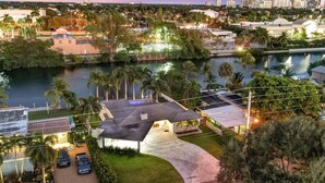 A modern house with a large patio, a swimming pool, and a view of the city skyline at dusk. - Lakefront Family Fun Home with Private Dock 3BR 2B (Fort Lauderdale)