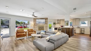 A spacious living room with a grey sectional sofa, a brown leather chair, and a small coffee table. A ceiling fan and recessed lighting are visible. - Lakefront Family Fun Home with Private Dock 3BR 2B (Fort Lauderdale)