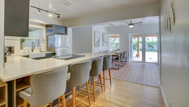 A modern kitchen with a central island, bar stools, and a dining area with a large table and chairs. - Tranquil Poolside Bliss + Pergola Deck & Turf Yard (Fort Lauderdale)