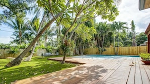 A wooden deck with a pool, surrounded by lush greenery and palm trees. - Tranquil Poolside Bliss + Pergola Deck & Turf Yard (Fort Lauderdale)