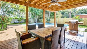 An outdoor patio with a wooden deck, a table with wicker chairs, a ceiling fan, and a barbecue grill. - Tranquil Poolside Bliss + Pergola Deck & Turf Yard (Fort Lauderdale)