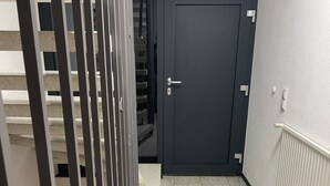 A narrow hallway with a dark door, a metal gate, and a tiled floor. - Kellerwohnung (Seelbach)