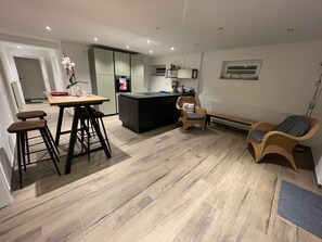 Una cocina moderna con una isla central, taburetes de bar, una silla de mimbre y un banco.