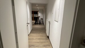 A narrow hallway with wooden flooring and white walls, leading to a dining area with a table and chairs. - Kellerwohnung (Seelbach)