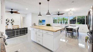 A modern kitchen with a central island, pendant lighting, ceiling fans, and large windows offering a view of the outdoors. - Wilton on the Water -Courtyard & Heated Pool 4/2.5 (Wilton Manors)
