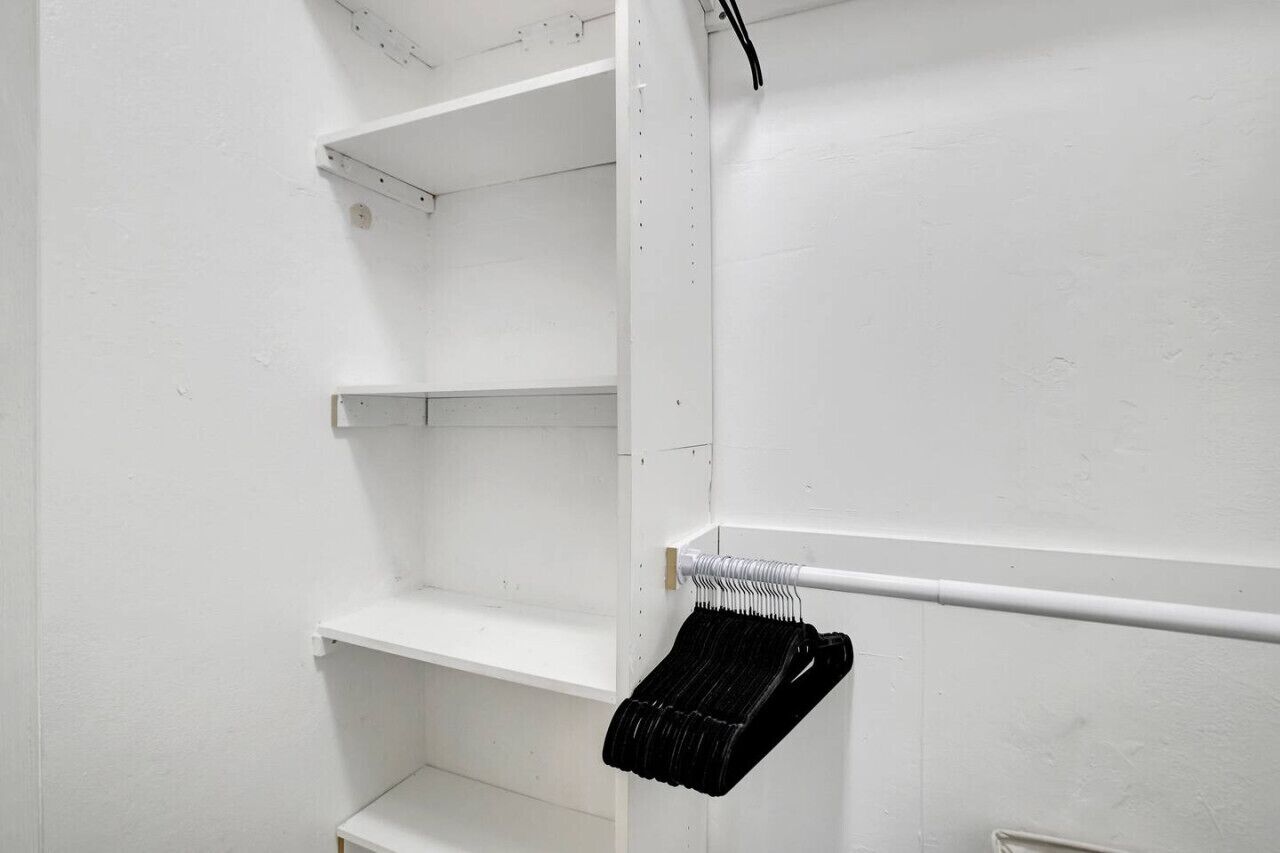 Un interior blanco con una estructura metálica que contiene objetos negros, paredes blancas y una puerta blanca.