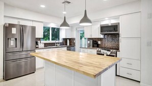 A modern kitchen with stainless steel appliances, white cabinetry, a wooden island, and pendant lighting. - Wilton on the Water -Courtyard & Heated Pool 4/2.5 (Wilton Manors)