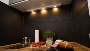 Una cocina con encimera de madera, un lavamanos, tabla de cortar con tomates, hogaza de pan, planta en maceta y un rollo de toallas de papel.